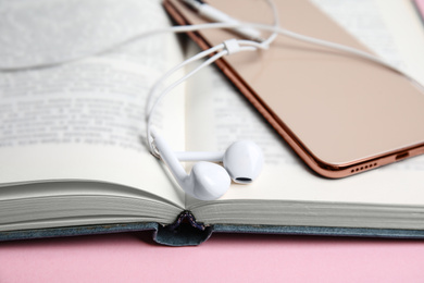 Book, headphones and smartphone on pink background, closeup