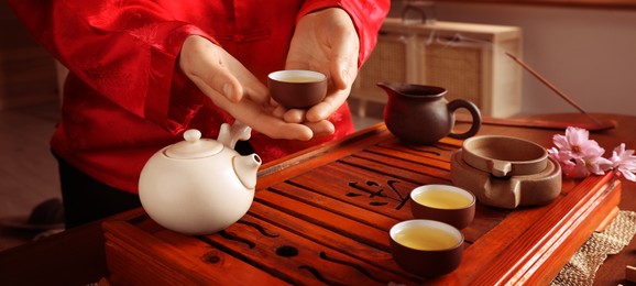 Image of Guest holding cup of freshly brewed tea during traditional ceremony at table indoors, closeup. Banner design