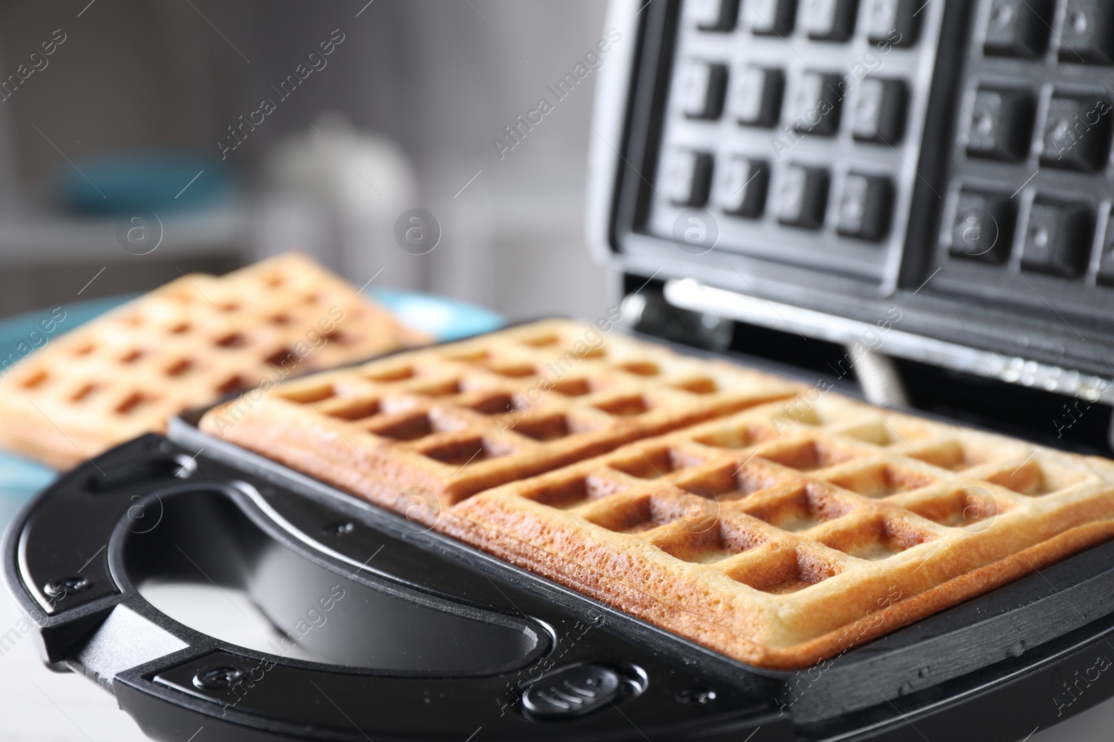 Photo of Modern iron with tasty Belgian waffles on table, closeup