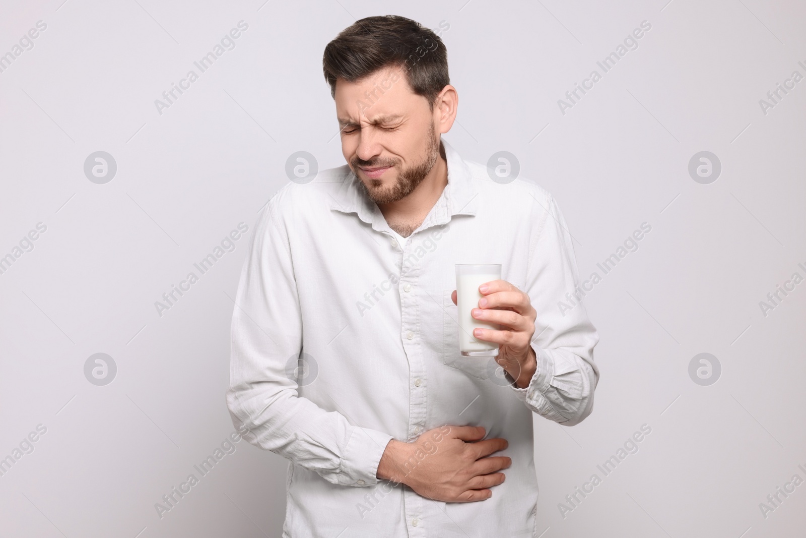 Photo of Man with glass of milk suffering from lactose intolerance on white background