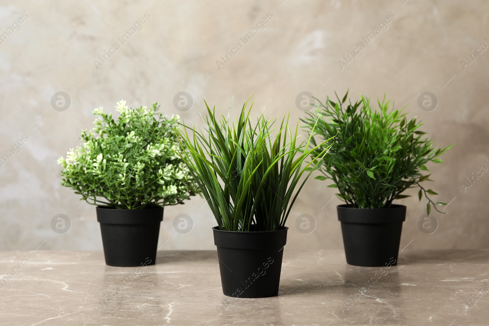 Photo of Beautiful artificial plants in flower pots on marble table