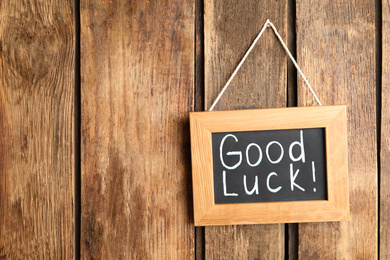 Photo of Blackboard with phrase GOOD LUCK hanging on wooden wall. Space for text