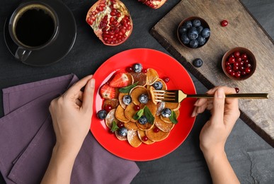 Photo of Woman eating cereal pancakes with blueberries at black table, top view