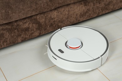 Robotic vacuum cleaner on white tiled floor near sofa indoors