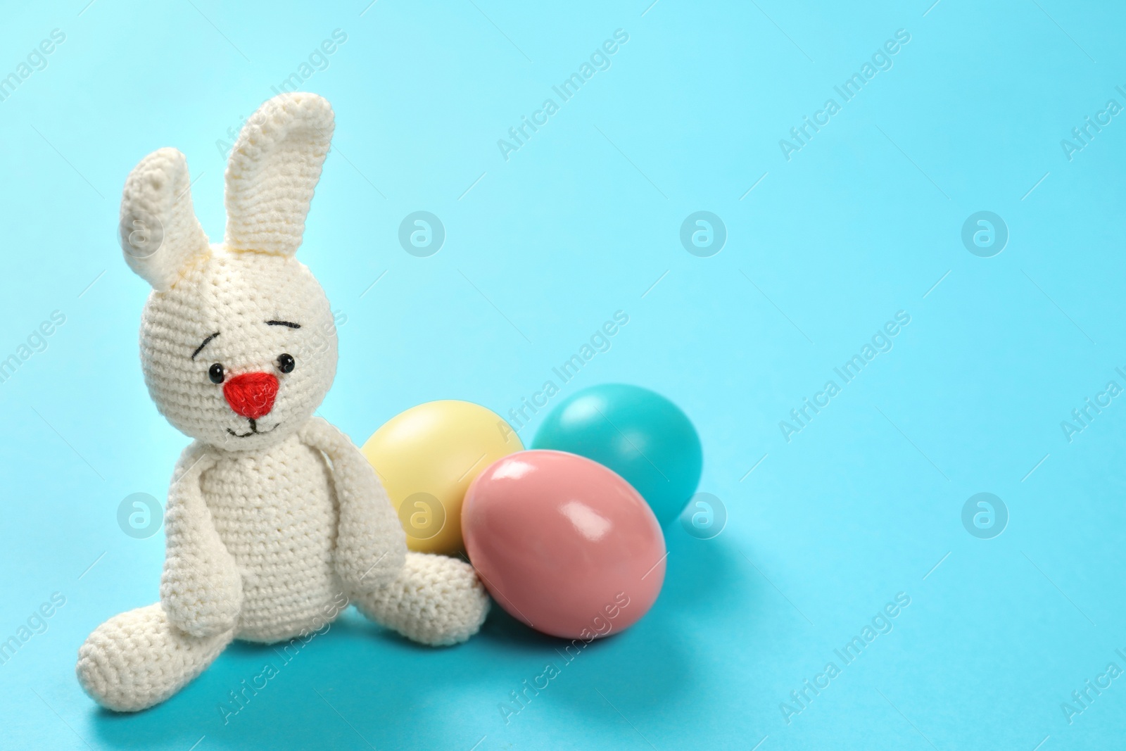 Photo of Cute Easter bunny toy and dyed eggs on color background, space for text