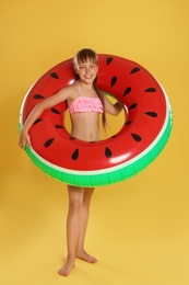 Cute little girl with bright inflatable ring on yellow background