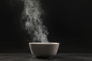 Photo of Steaming ceramic bowl on grey table against dark background