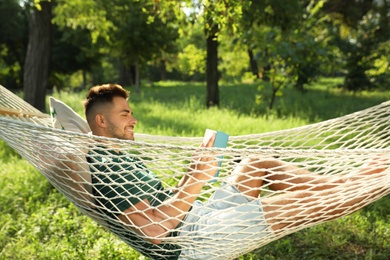 Young man reading book in comfortable hammock at green garden
