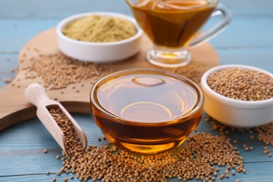 Photo of Bowl of natural oil, mustard seeds and powder on light blue wooden table, closeup