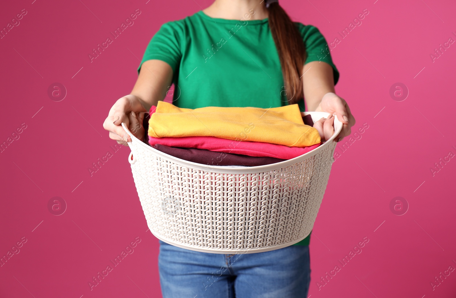 Photo of Young woman holding basket with laundry on color background, closeup