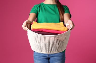 Young woman holding basket with laundry on color background, closeup