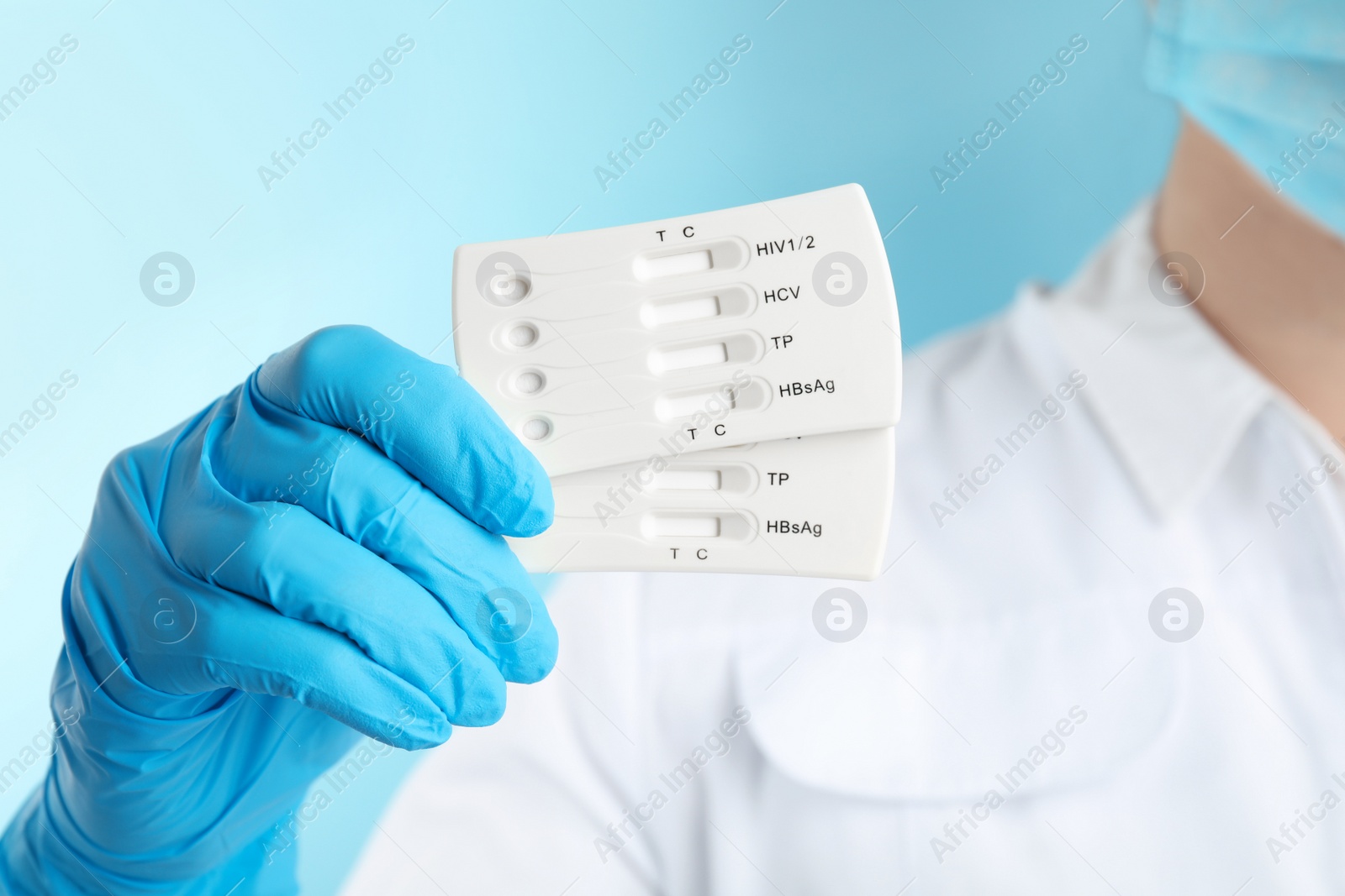 Photo of Doctor holding two disposable express tests for hepatitis on light blue background, closeup