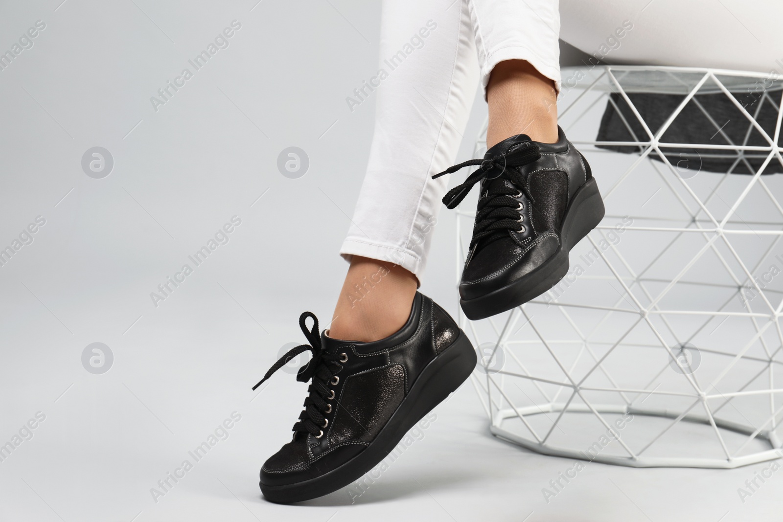 Photo of Woman in stylish shoes sitting on stool, grey background. Space for text