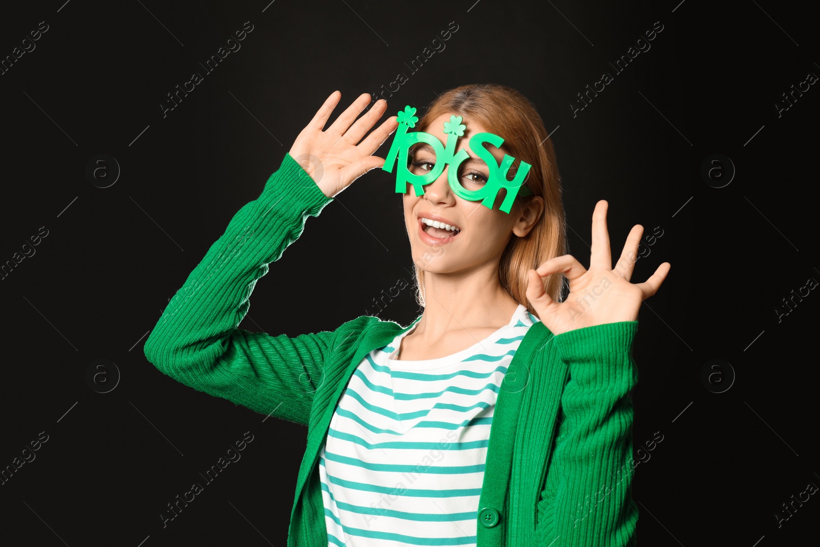 Photo of Young woman with party glasses on black background. St. Patrick's Day celebration