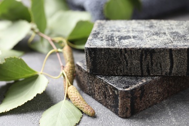 Photo of Natural tar soap and birch branch on grey stone table, closeup
