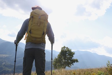 Photo of Tourist with backpack and trekking poles enjoying mountain landscape, back view. Space for text