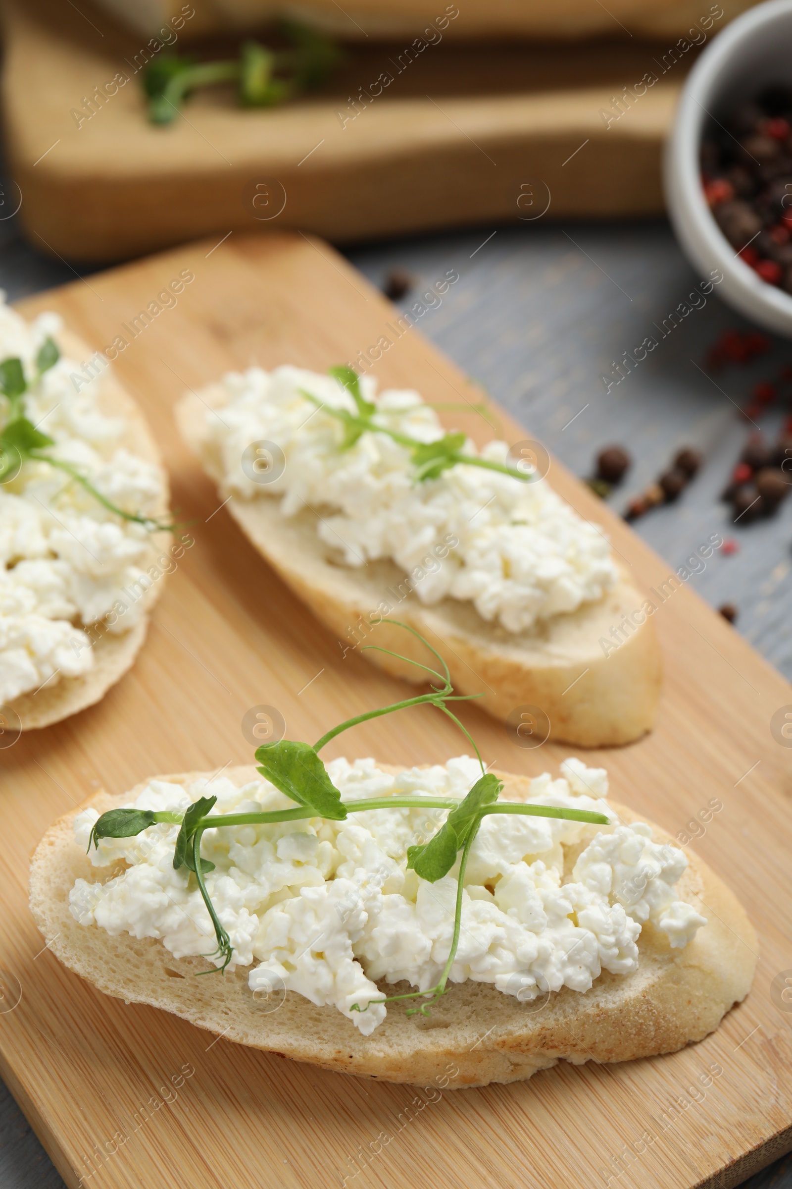 Photo of Bread with cottage cheese and microgreens on wooden board, closeup