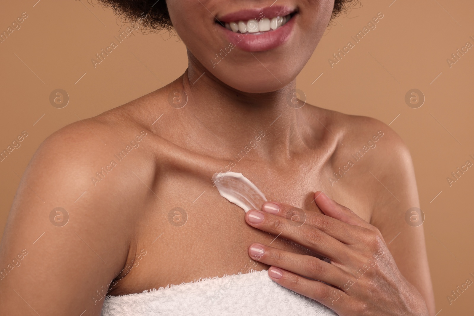 Photo of Young woman applying cream onto body on beige background, closeup