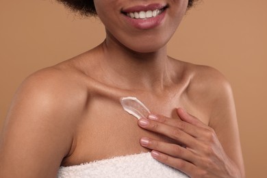 Photo of Young woman applying cream onto body on beige background, closeup