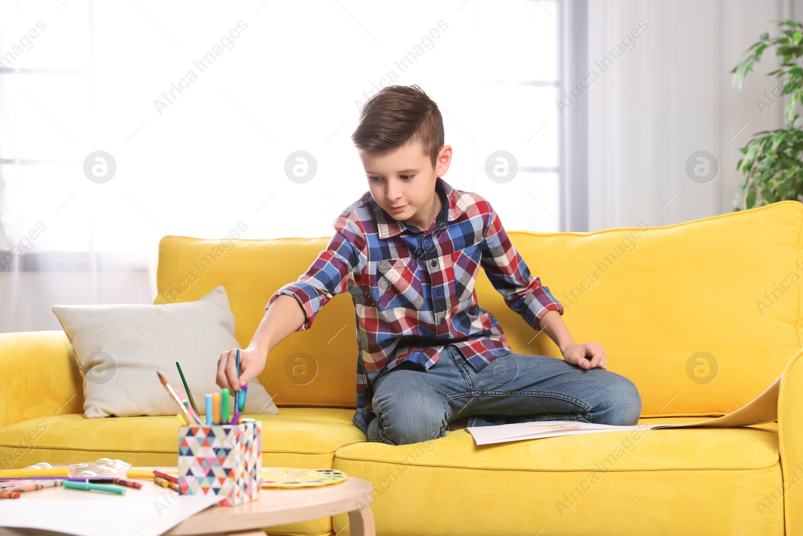 Photo of Little boy painting picture on sofa indoors