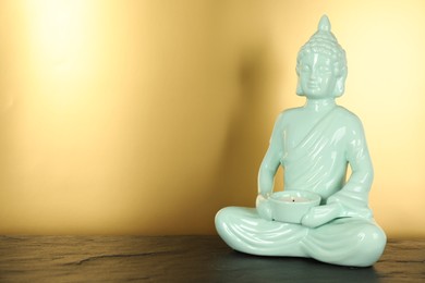 Buddha statue with burning candle on black table. Space for text