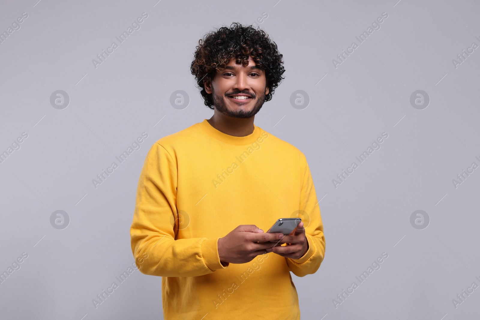 Photo of Handsome smiling man using smartphone on light grey background, space for text