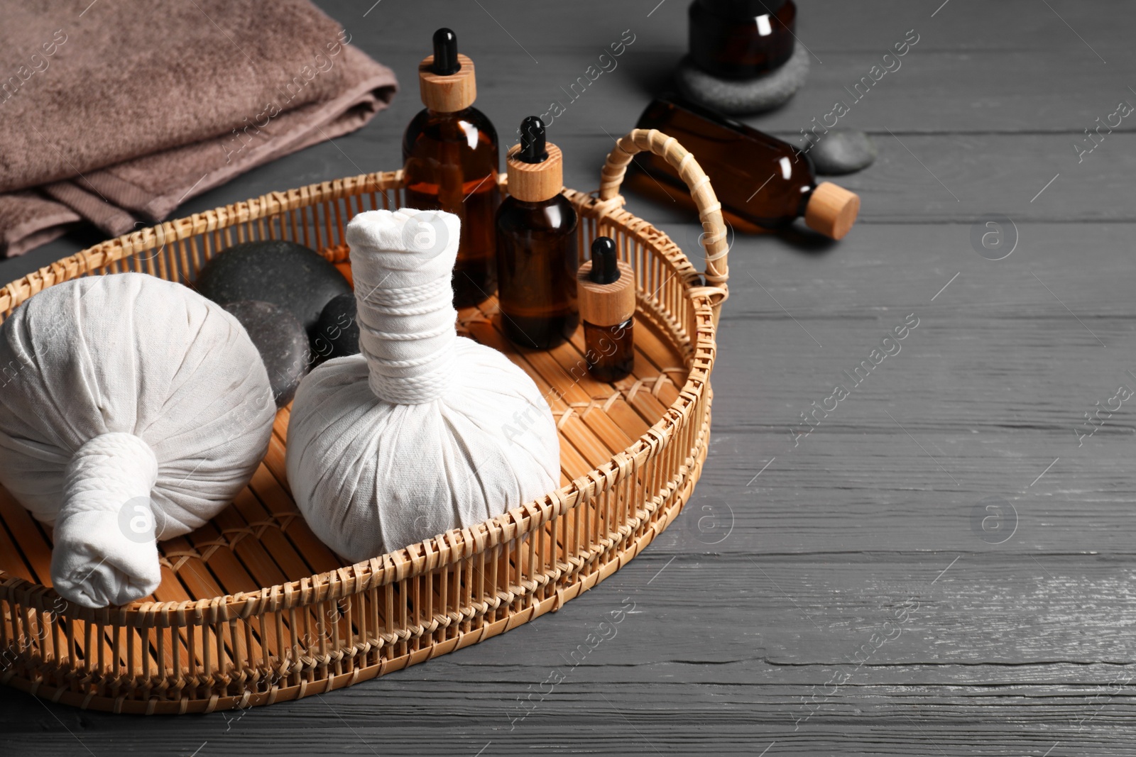 Photo of Herbal massage bags, essential oils and spa stones on grey wooden table, space for text