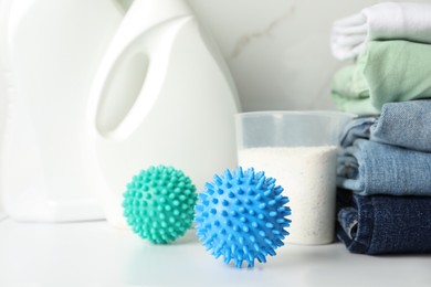 Photo of Dryer balls, stacked clean clothes and detergents on white table