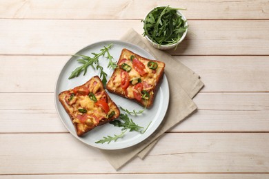 Photo of Tasty pizza toasts and fresh arugula on light wooden table, flat lay