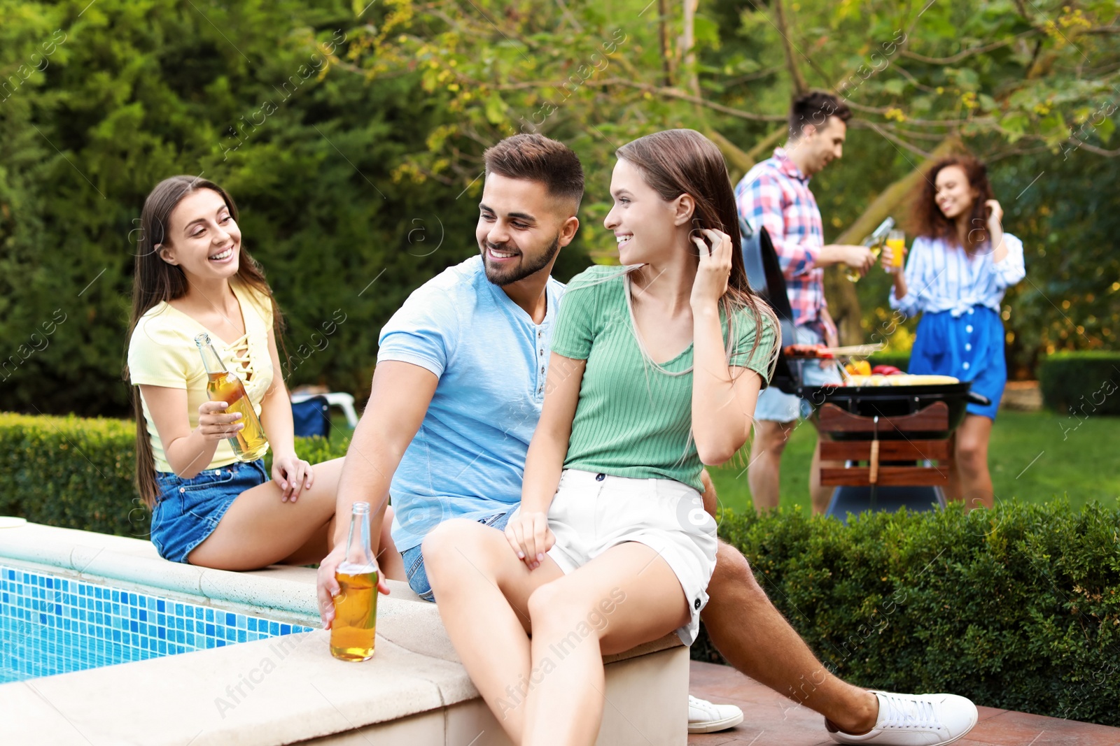 Photo of Happy friends with drinks at barbecue party near swimming pool outdoors