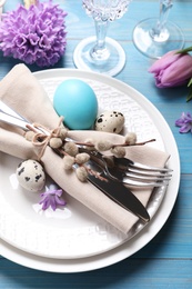 Festive Easter table setting with  painted eggs and floral decor on light blue wooden background