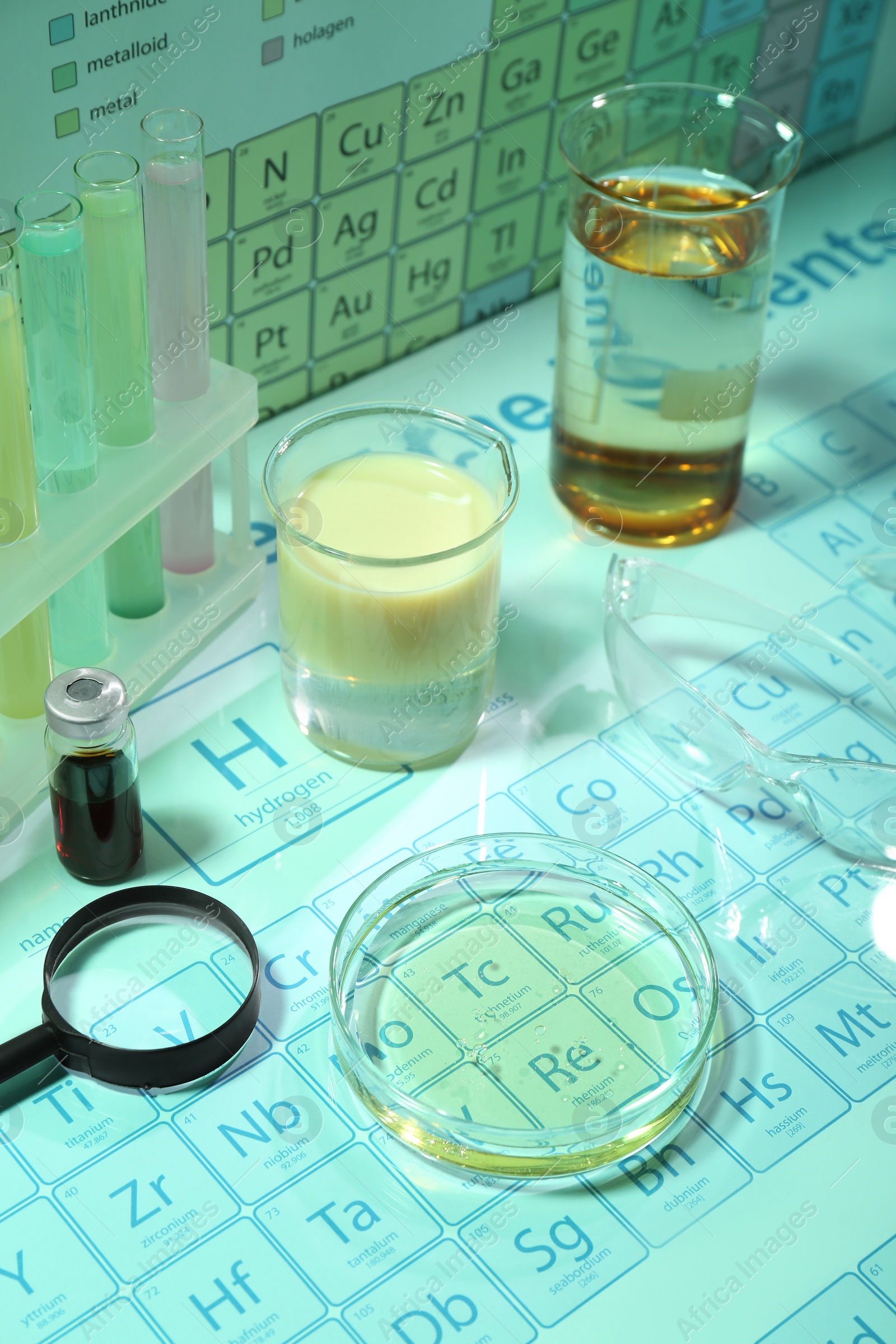 Photo of Different laboratory equipment with liquids and safety glasses on periodic table of chemical elements. Light green tone effect