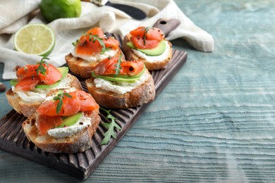 Delicious sandwiches with cream cheese, salmon, avocado and arugula on light blue wooden table. Space for text