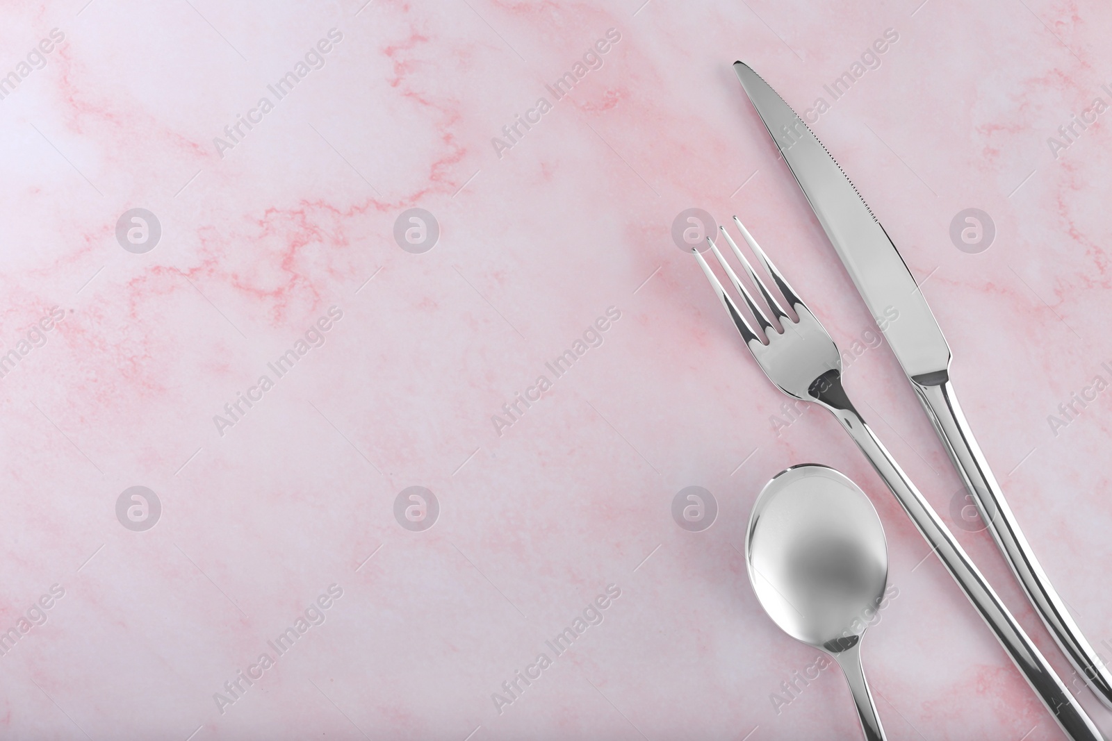 Photo of Stylish cutlery set on pink marble table, flat lay. Space for text