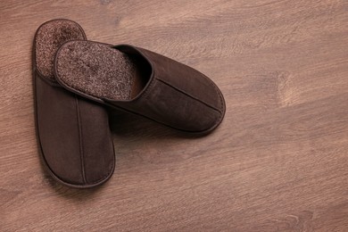 Photo of Pair of brown slippers on wooden floor, top view. Space for text