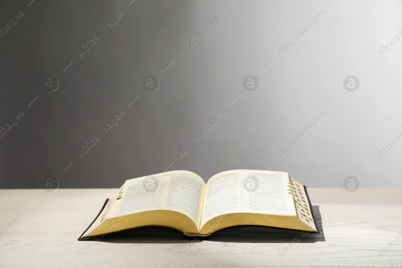 Photo of Open Bible on white wooden table against light grey background. Christian religious book