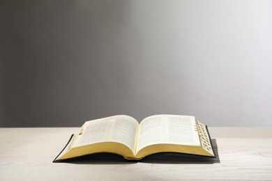 Photo of Open Bible on white wooden table against light grey background. Christian religious book