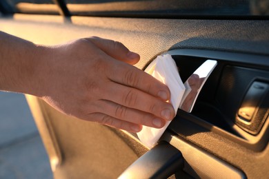 Man with napkin sanitizing car door handle, closeup