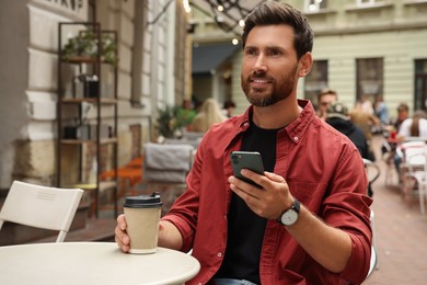 Handsome man with cup of coffee using smartphone in outdoor cafe