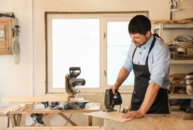 Photo of Mature working man using jigsaw at carpentry shop, space for text