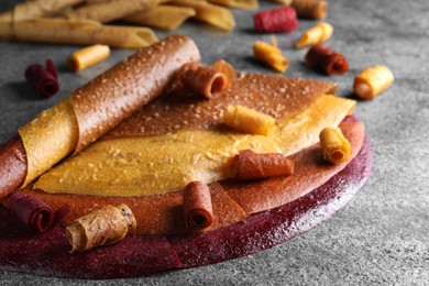 Delicious fruit leather rolls on grey table, closeup