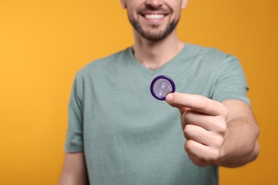Photo of Happy man holding condom on orange background, closeup