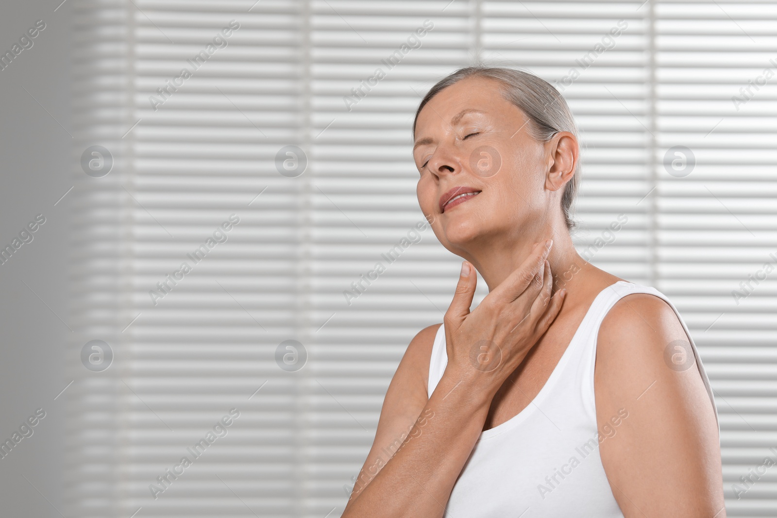 Photo of Happy woman applying body oil onto neck indoors. Space for text