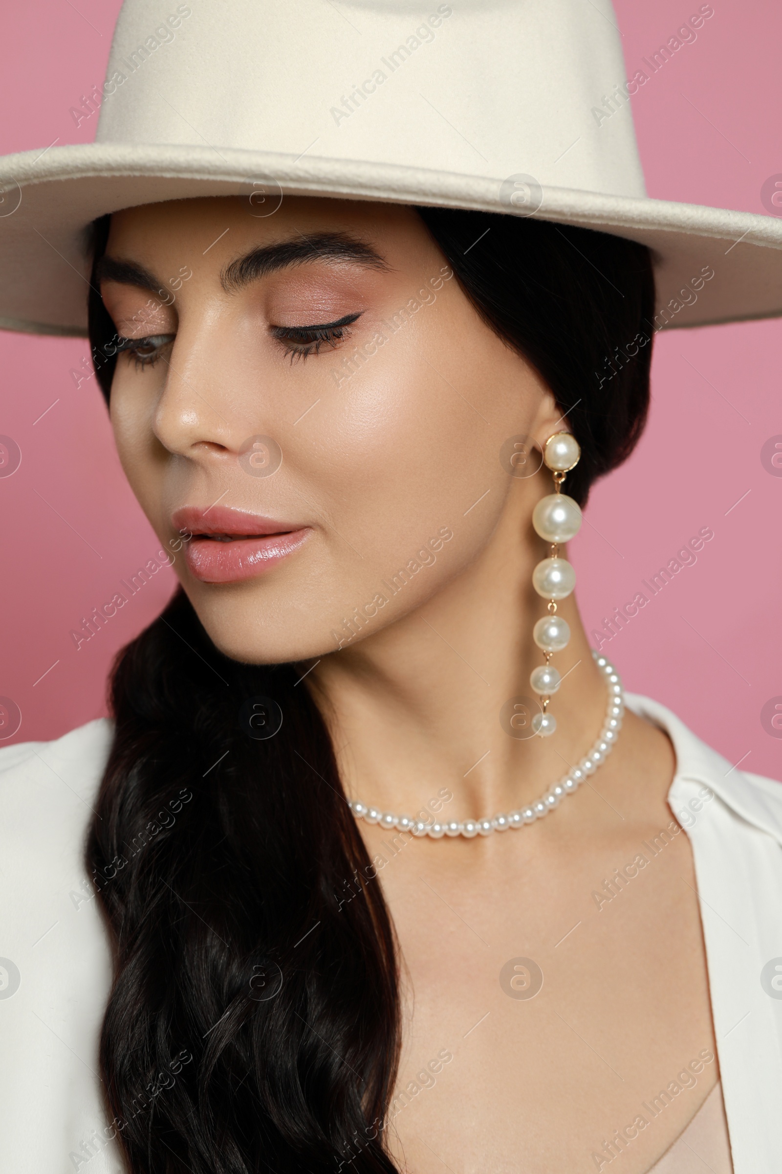 Photo of Young woman wearing elegant pearl jewelry on pink background, closeup