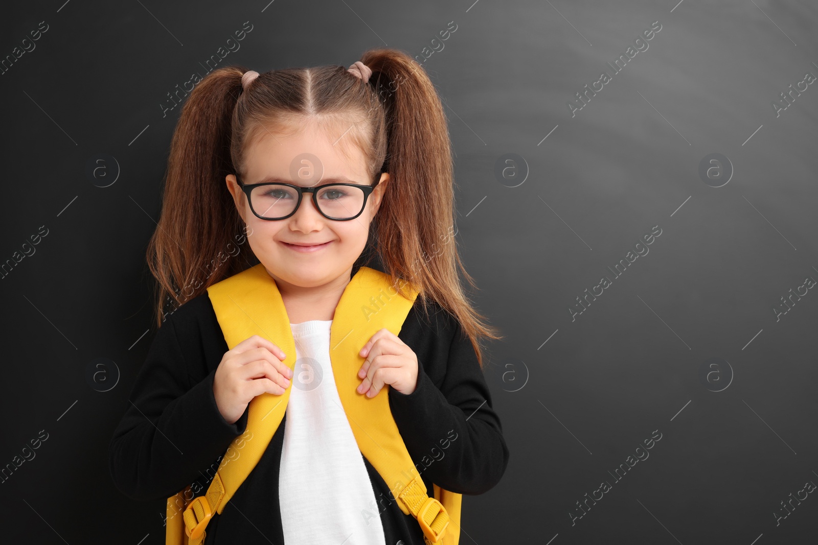 Photo of Happy little school child with backpack near chalkboard. Space for text