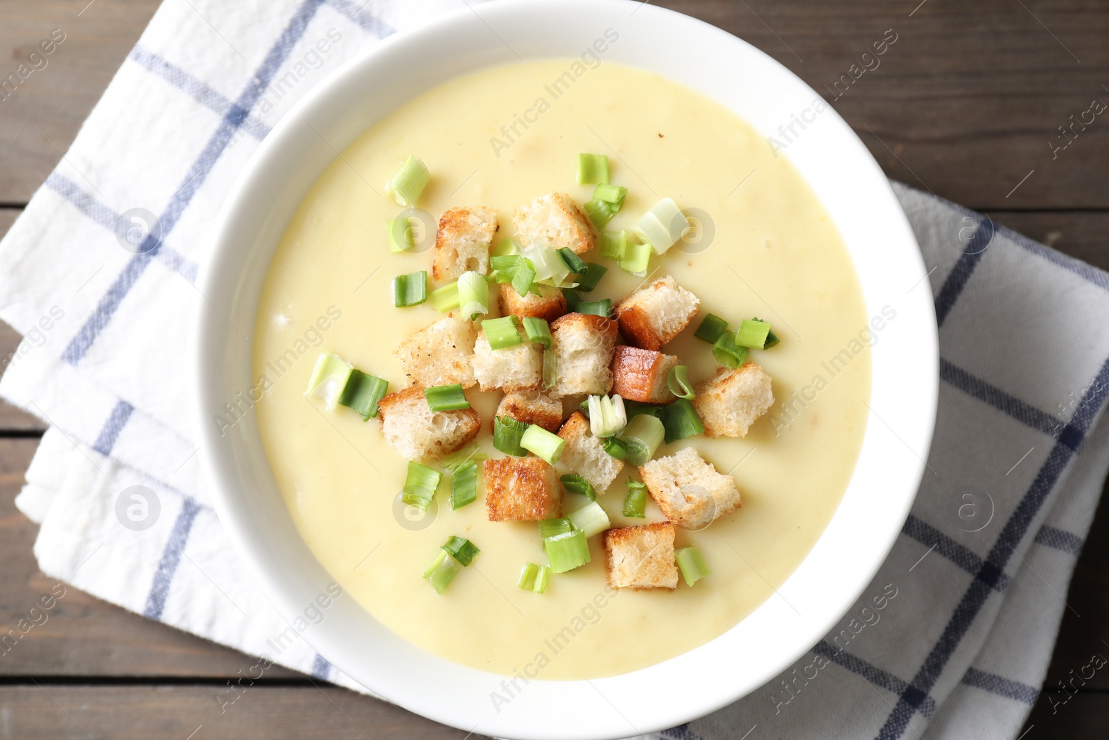 Photo of Tasty potato soup with croutons and green onion in bowl on wooden table, top view