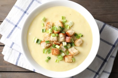 Photo of Tasty potato soup with croutons and green onion in bowl on wooden table, top view