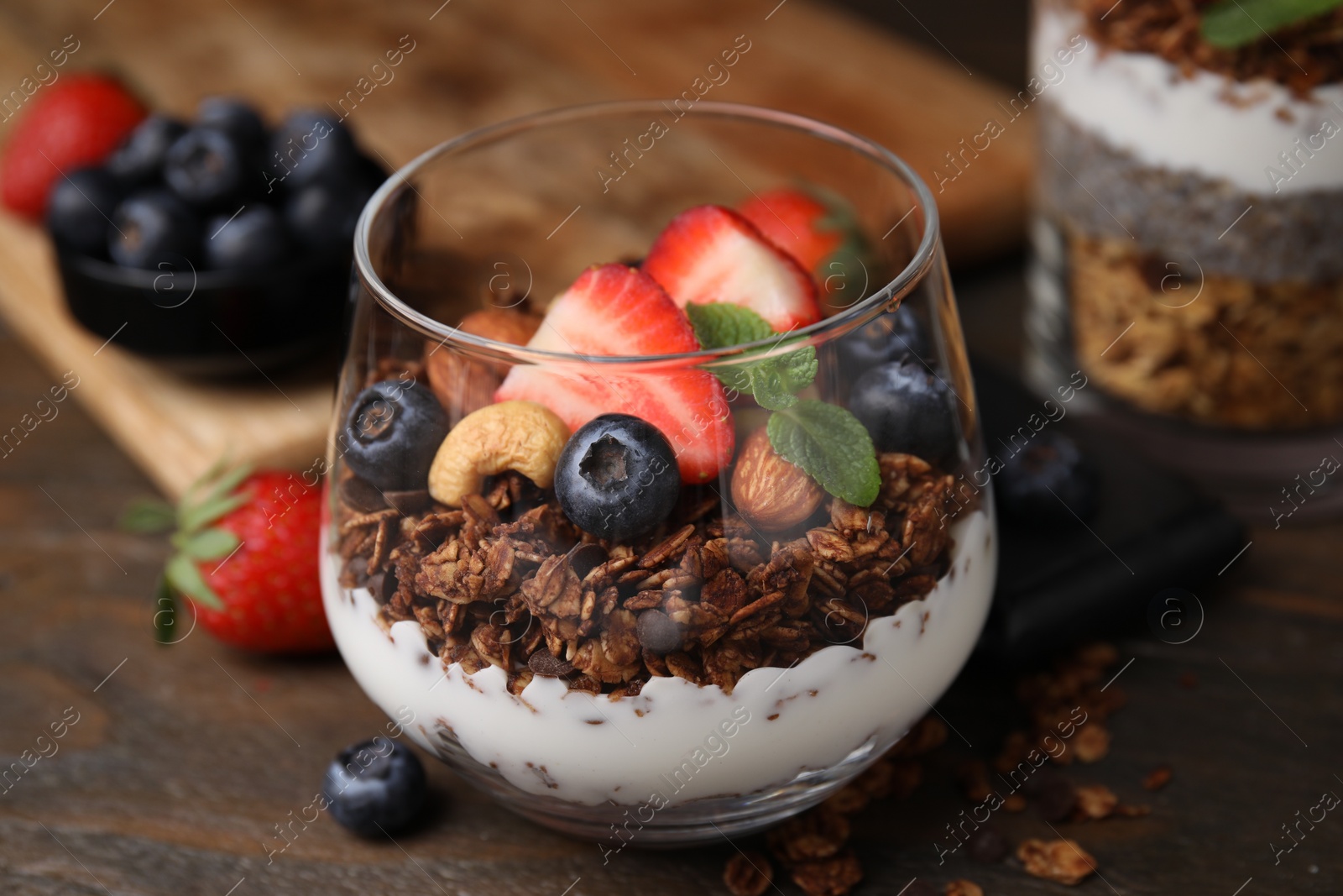 Photo of Tasty granola with berries, nuts and yogurt in glass on wooden table, closeup