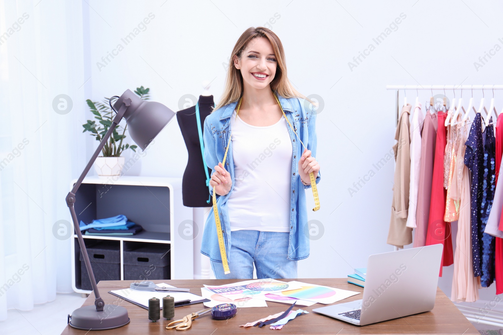 Photo of Beautiful young stylist at workplace near rack with clothes