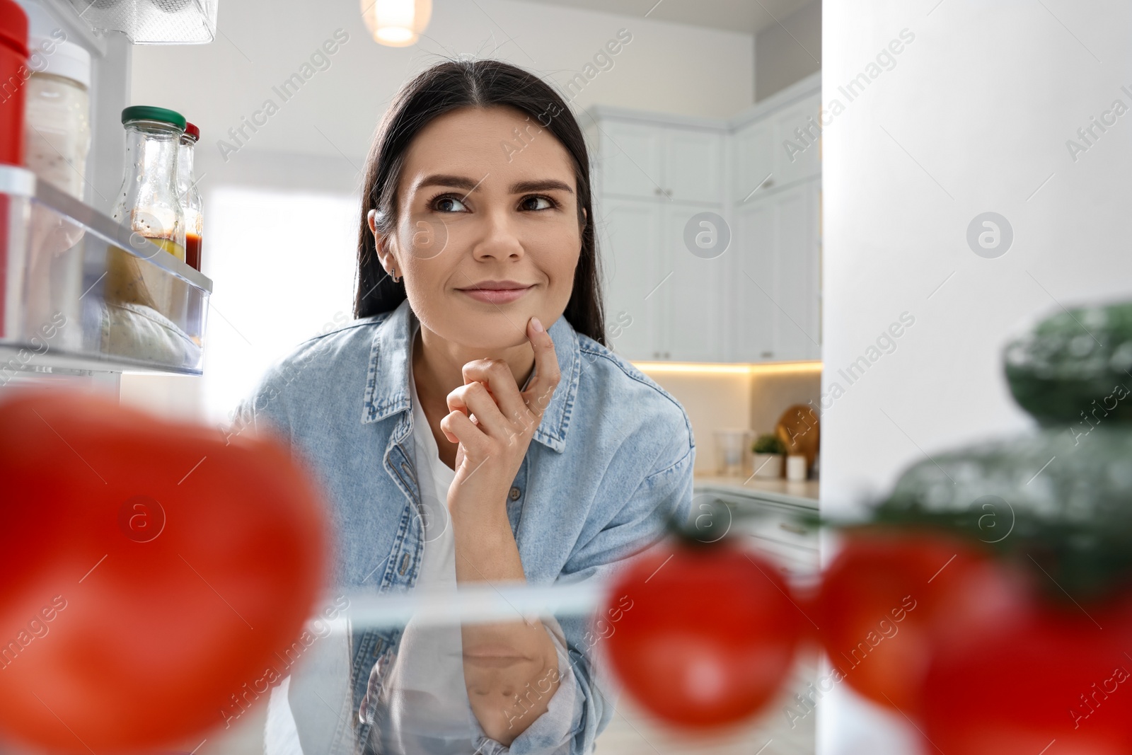 Photo of Young woman near refrigerator in kitchen, view from inside